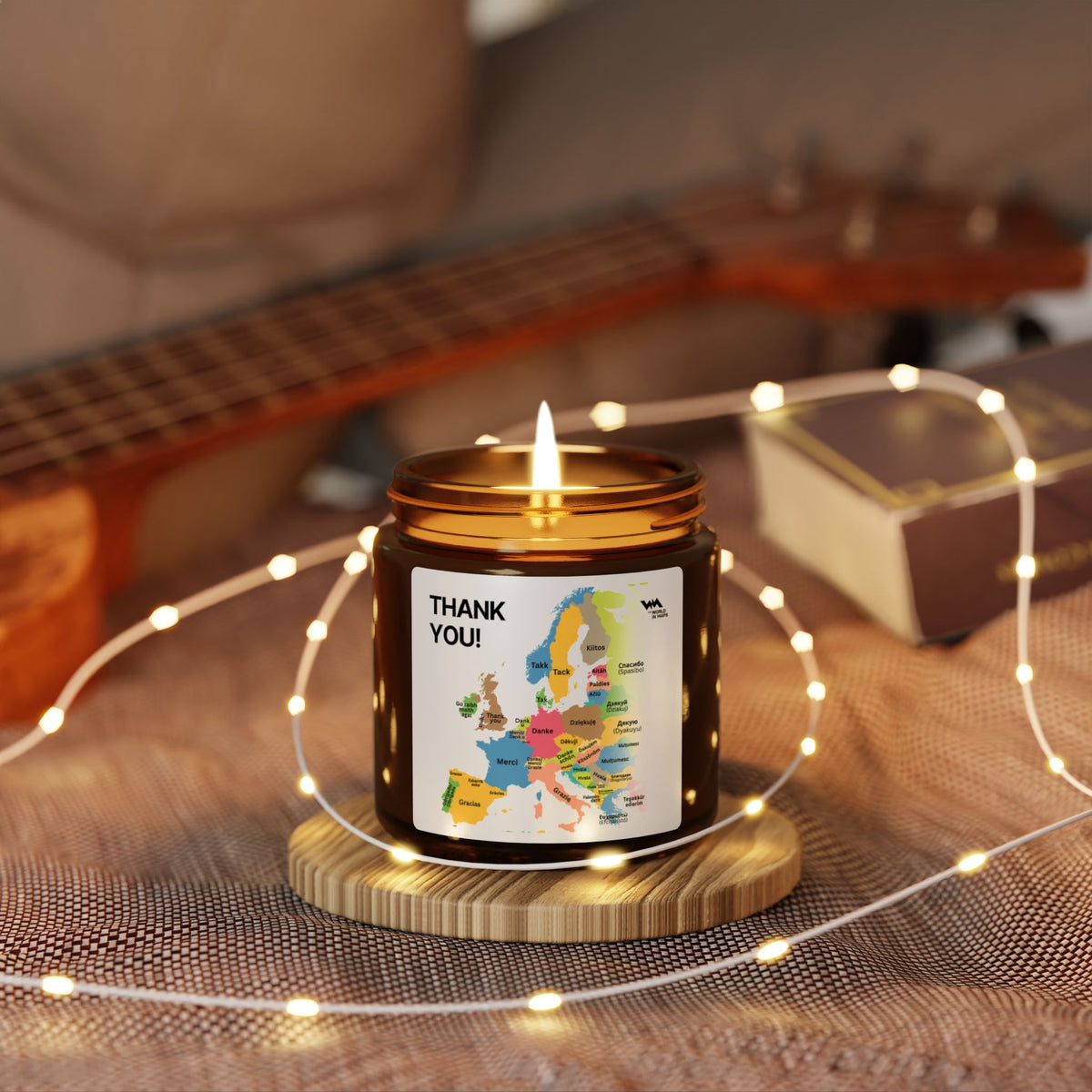 Lit Thank You map candle on a wooden coaster surrounded by fairy lights